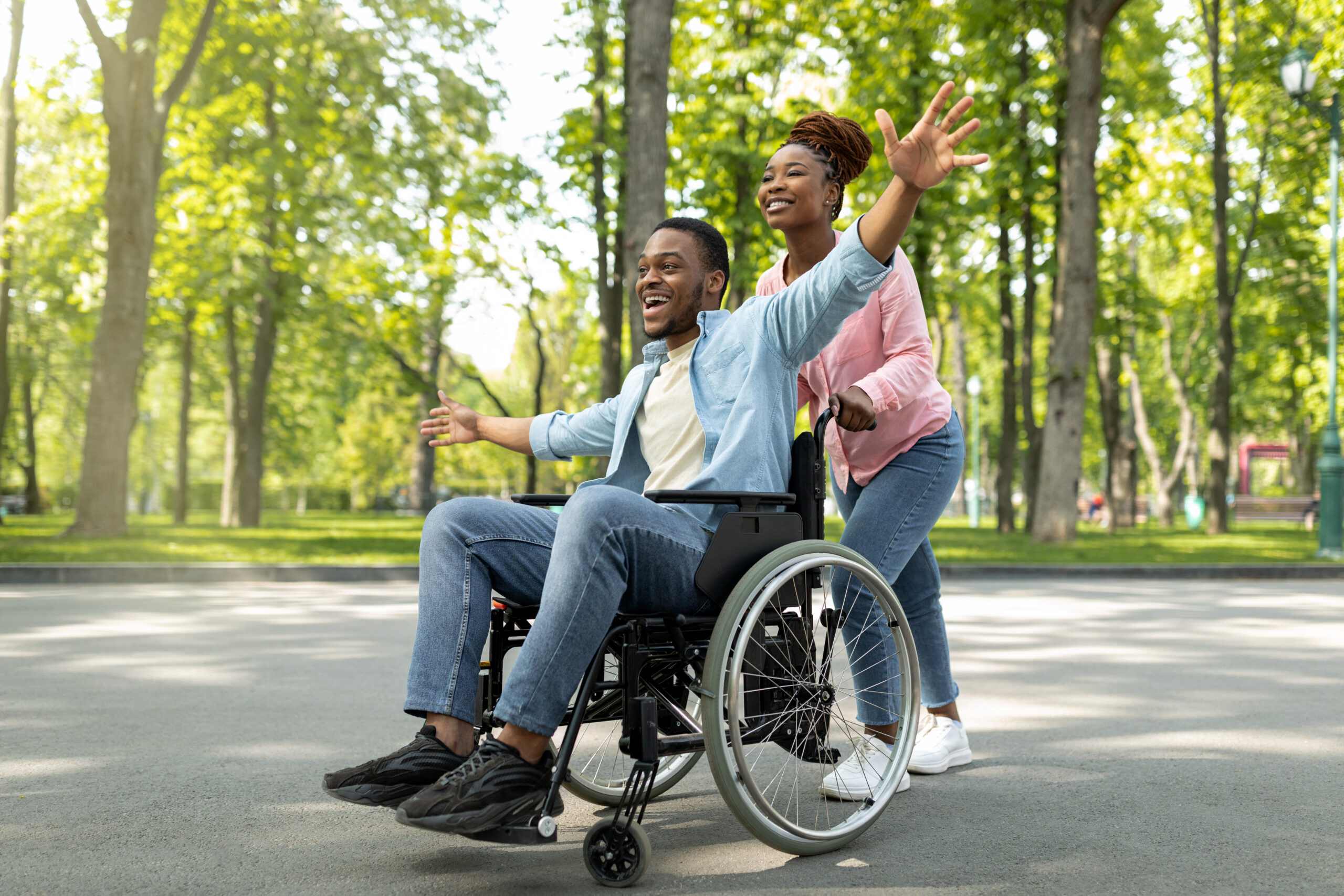 Happy Black Disabled Guy In Wheelchair On Walk With His Loving Girlfriend Outdoors Having Fun Spending Time Together